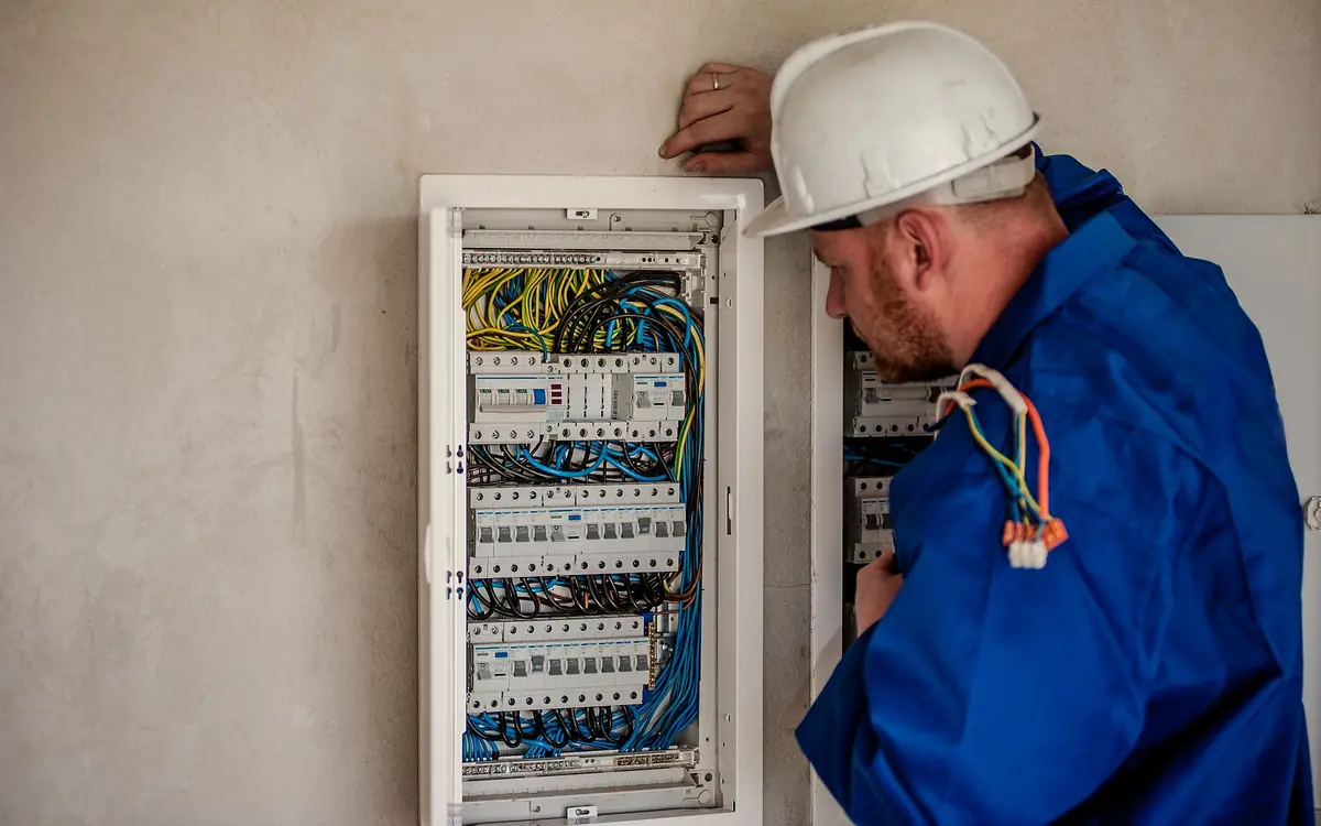 Electrician in a hard hat working on an open wall-mounted distribution board