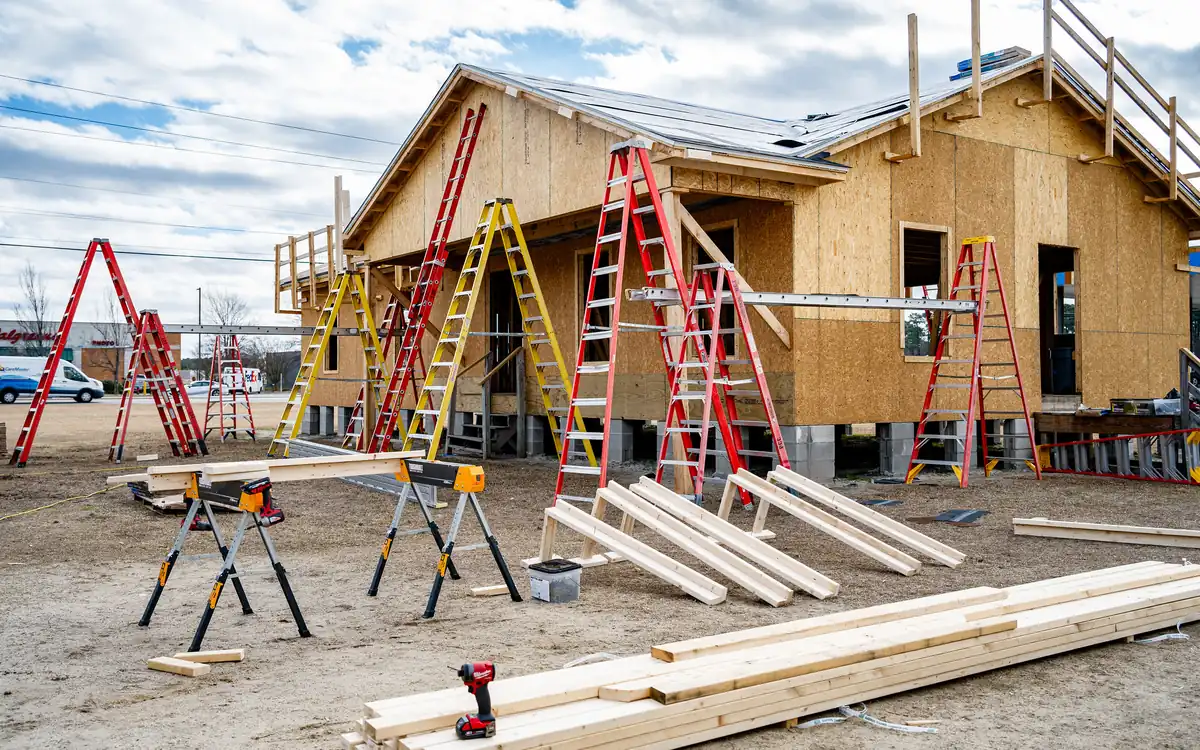Timber-framed house under construction with ladders, sawhorses and lumber