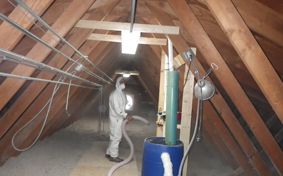 Worker in a protective suit blowing loose-fill insulation into an attic